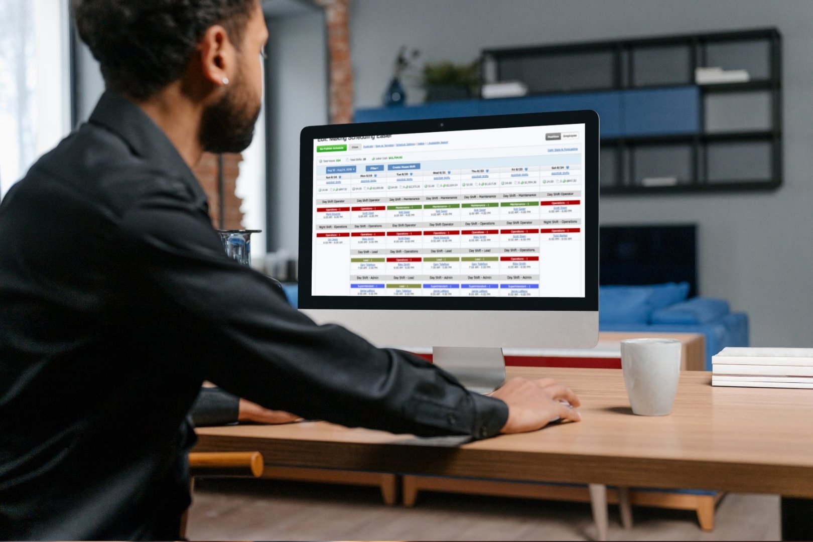 Man reviewing an automated employee shift schedule on a desktop computer in a modern office setting