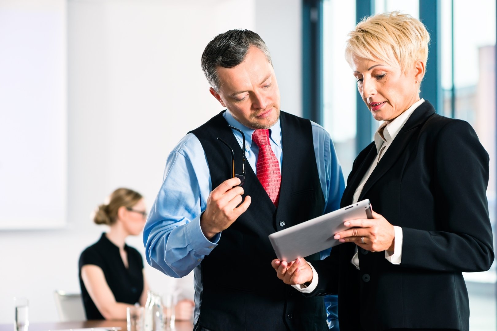 Two business professionals reviewing labor planning data on a digital tablet during a meeting, discussing smarter scheduling strategies.
