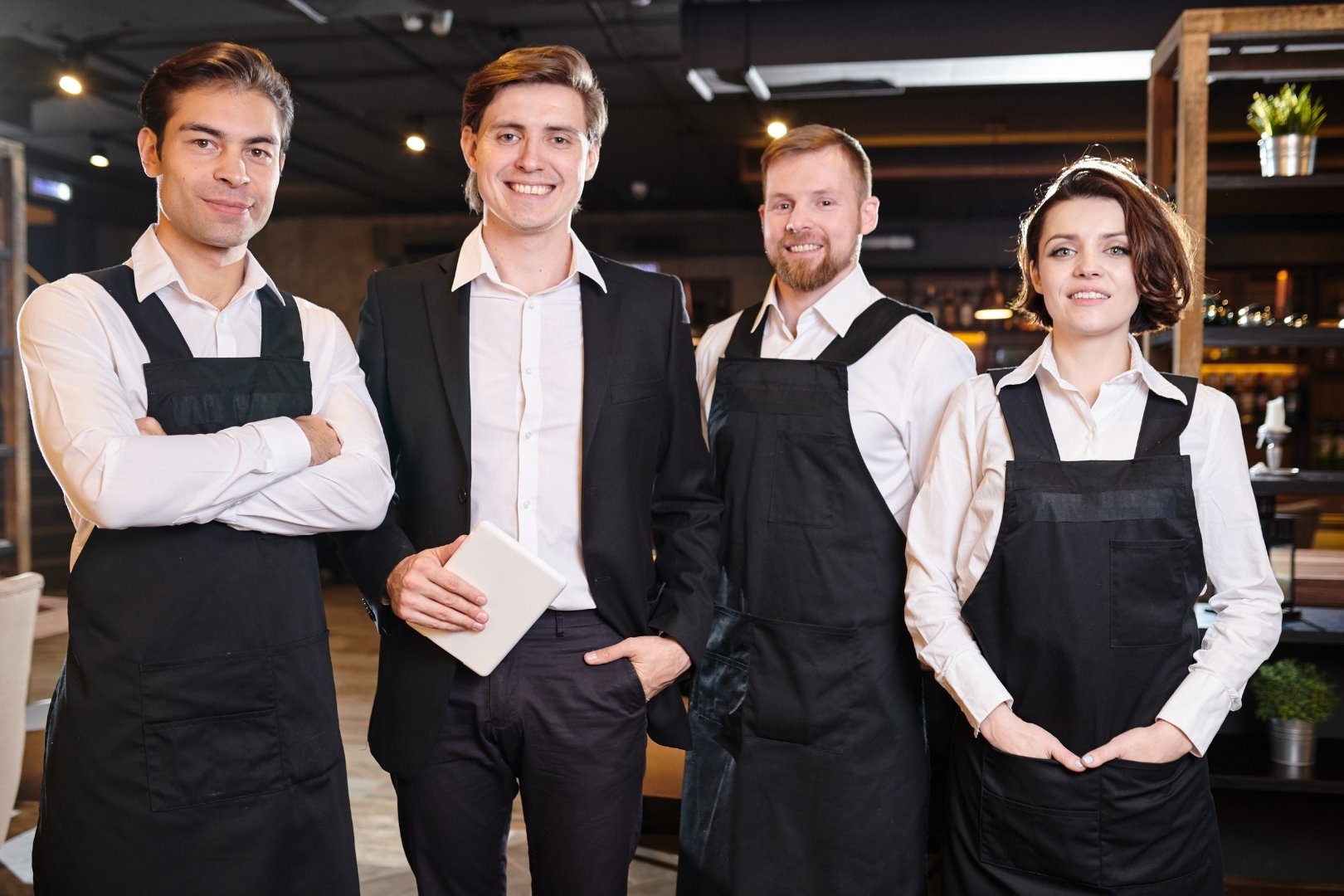 Shift manager with team in uniform smiling in a restaurant setting.